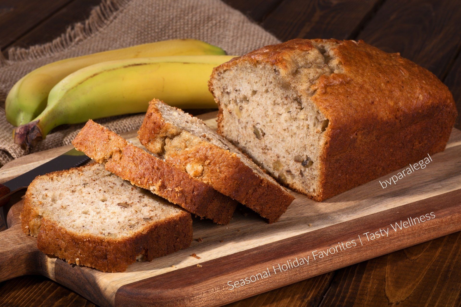 A loaf of banana bread is sitting on a wooden cutting board next to bananas.