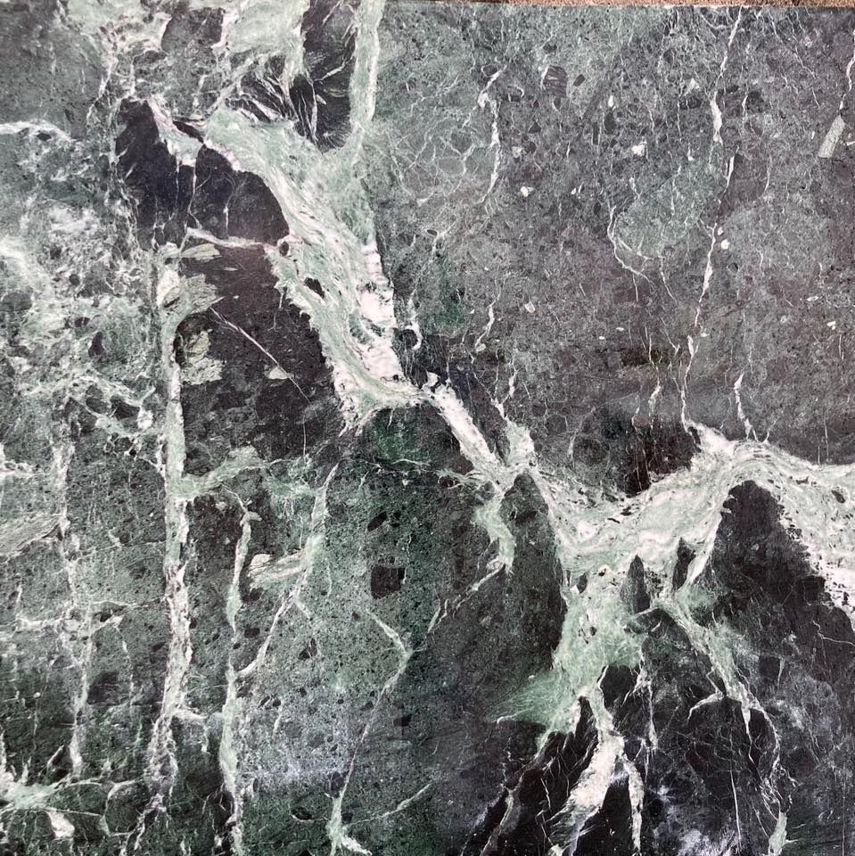 Camino angolare con marmo nero e venature dorate, posizionato su un pavimento in piastrelle beige e contro pareti bianche.