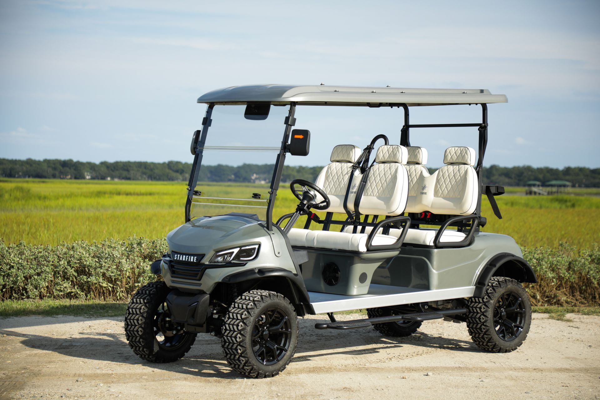 White golf cart parked on a dirt road beside green fields under a blue sky