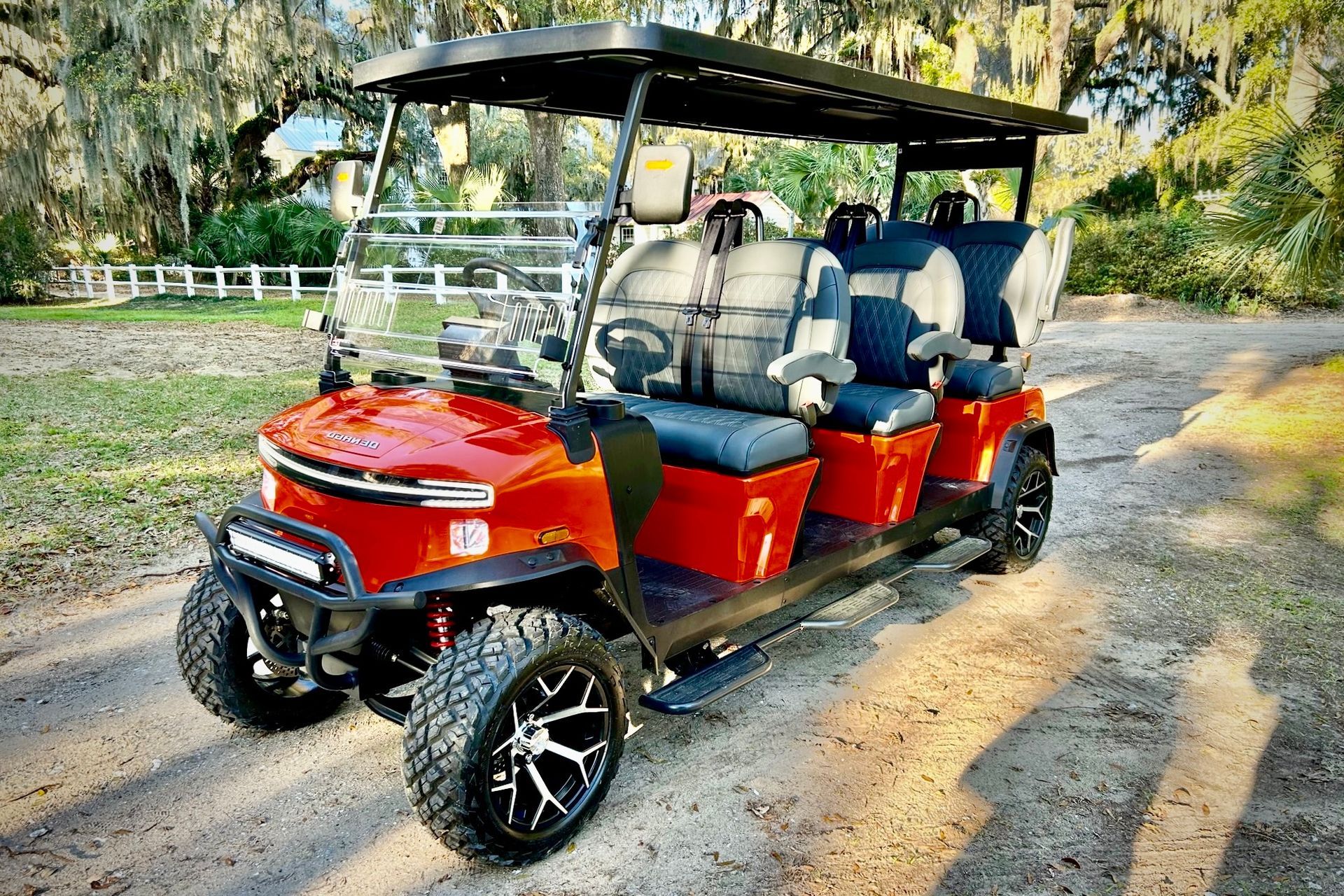 Red six-seat golf cart on a dirt path beside a white fence and trees.