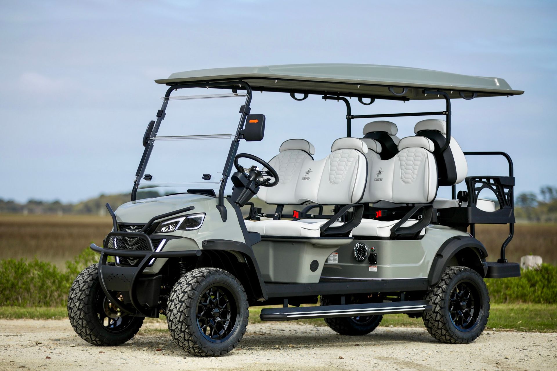 Gray four-seat golf cart with white seats parked on a dirt road in a rural field