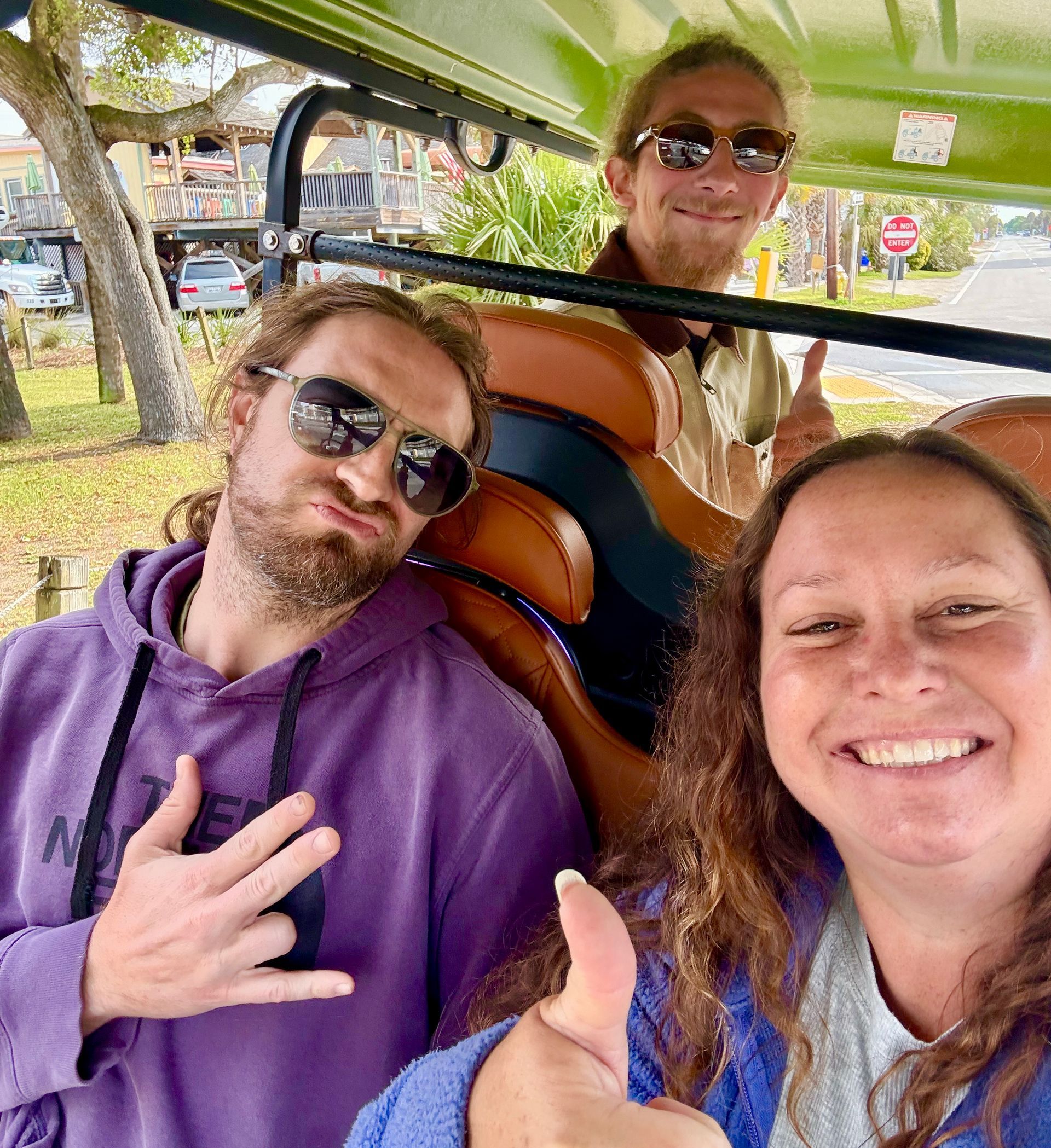 Three people smiling and giving hand gestures from inside a golf cart.