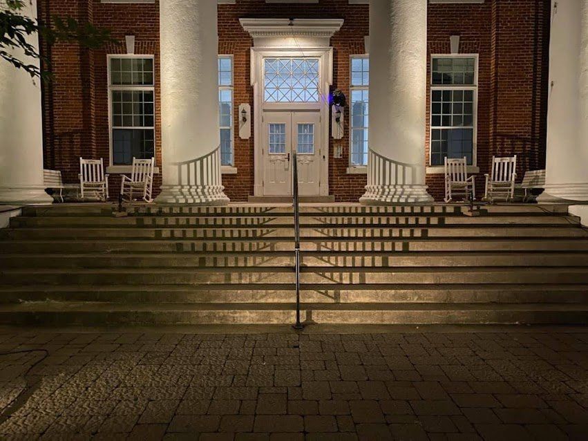 The front of a building with stairs and rocking chairs at night.