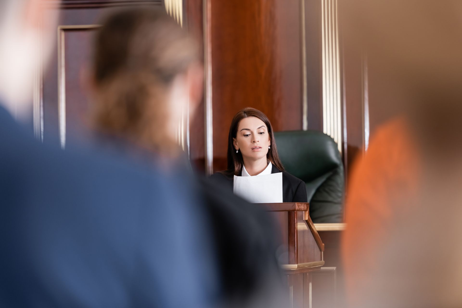 A female judge is sitting at a podium in a courtroom.