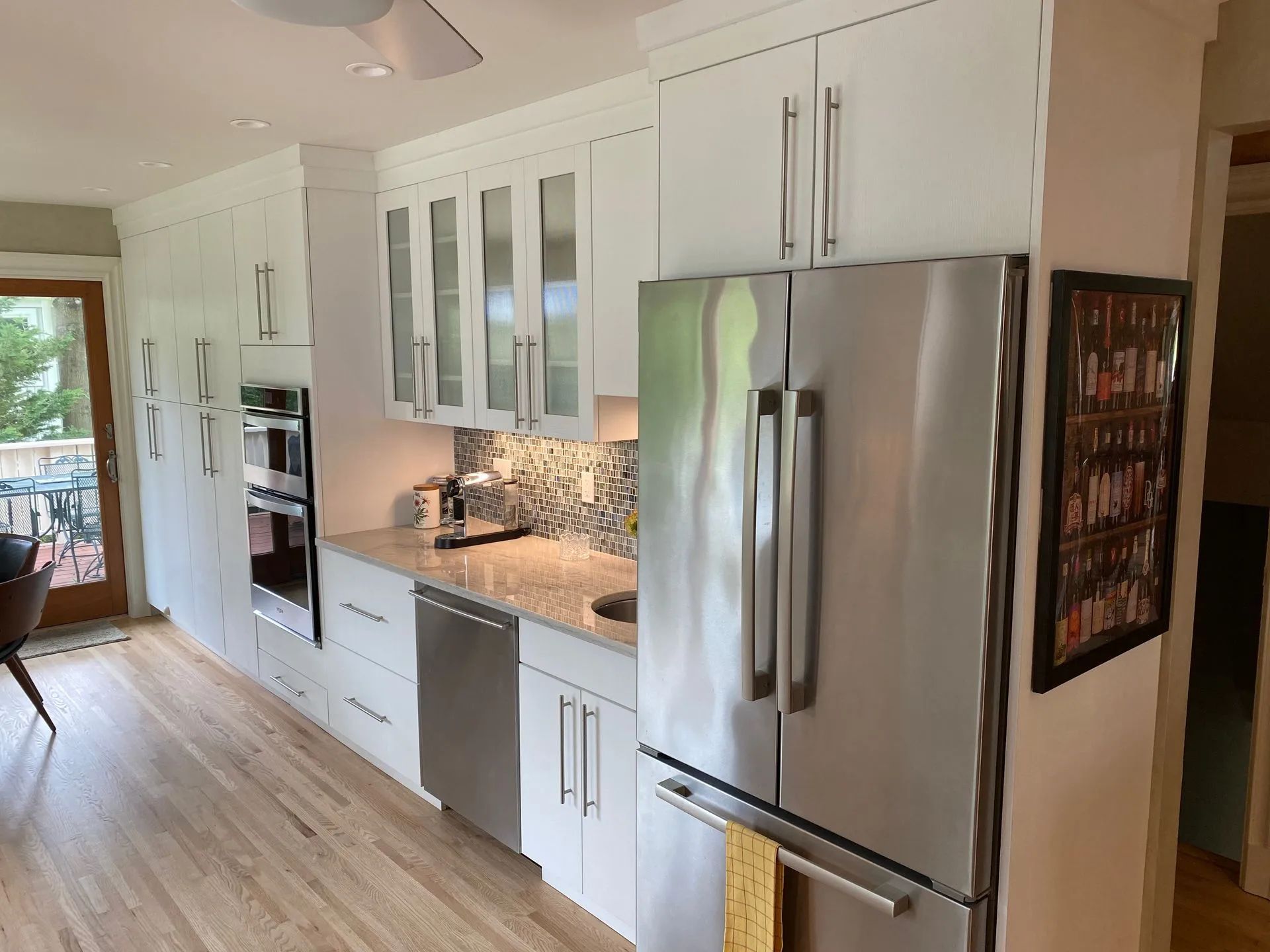 White kitchen with stainless steel appliances, light wood floors, and glass-front upper cabinets.
