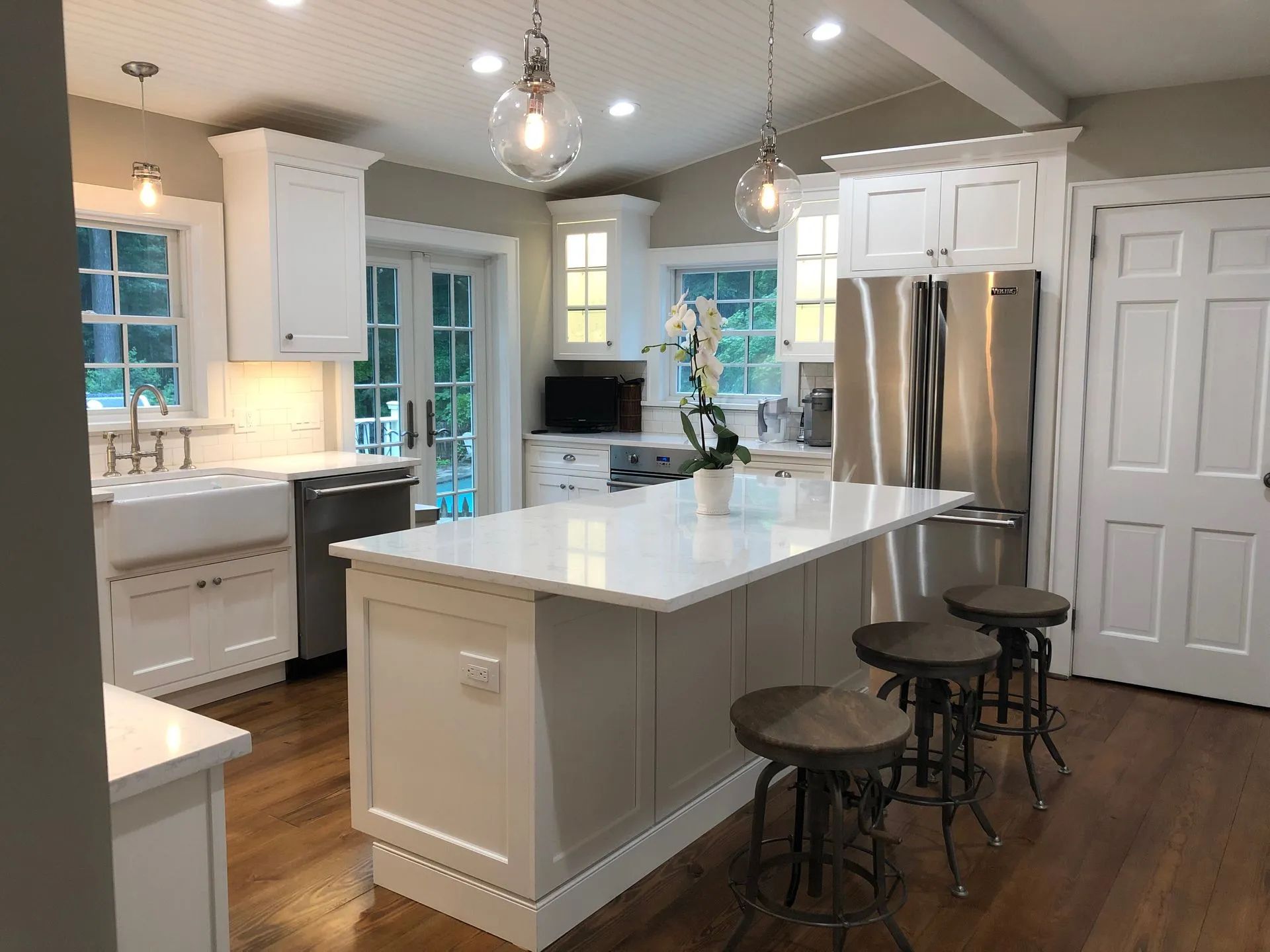 White kitchen with an island, stainless steel appliances, and wooden floors.