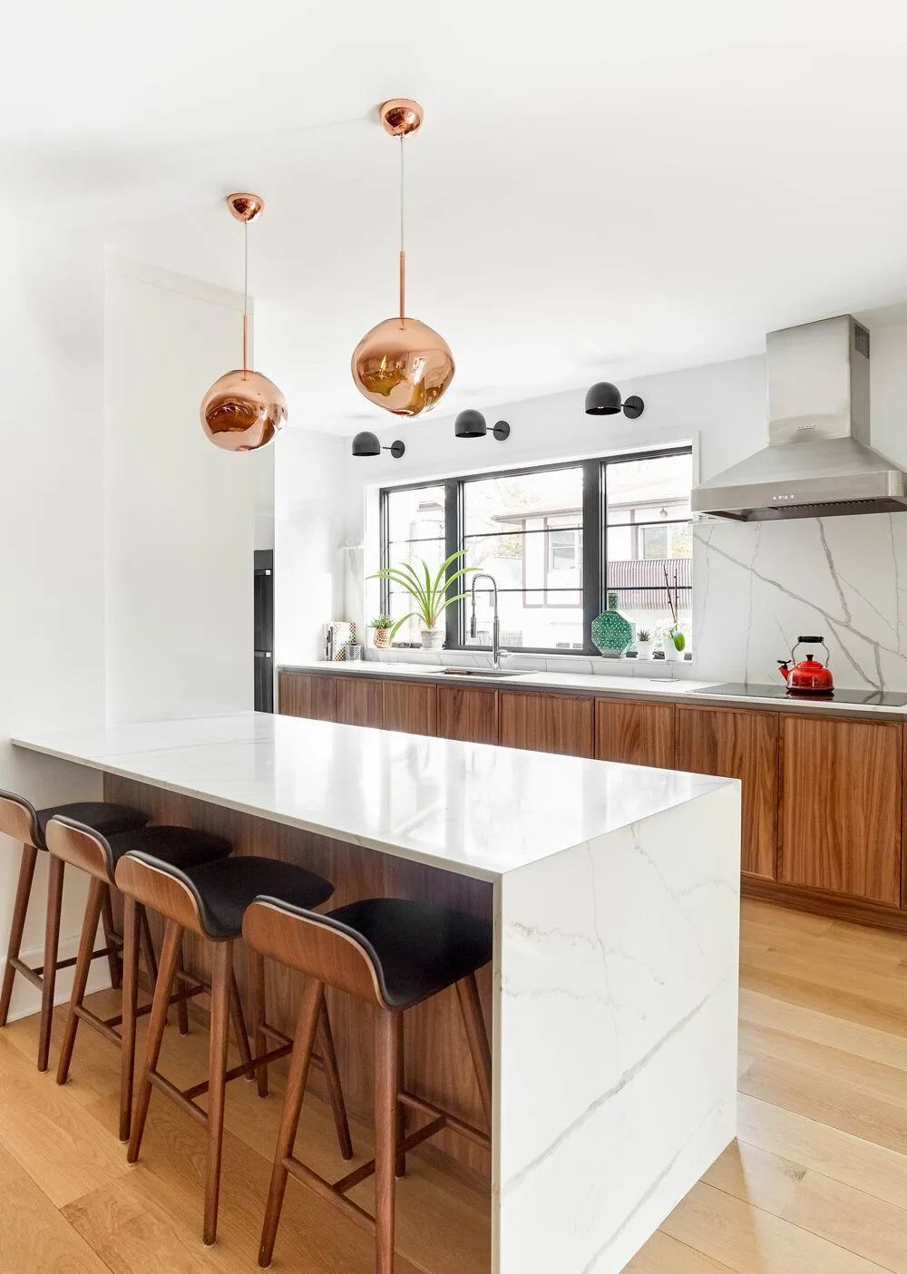 Modern kitchen with island, copper pendant lights, wood cabinets, and marble countertops.