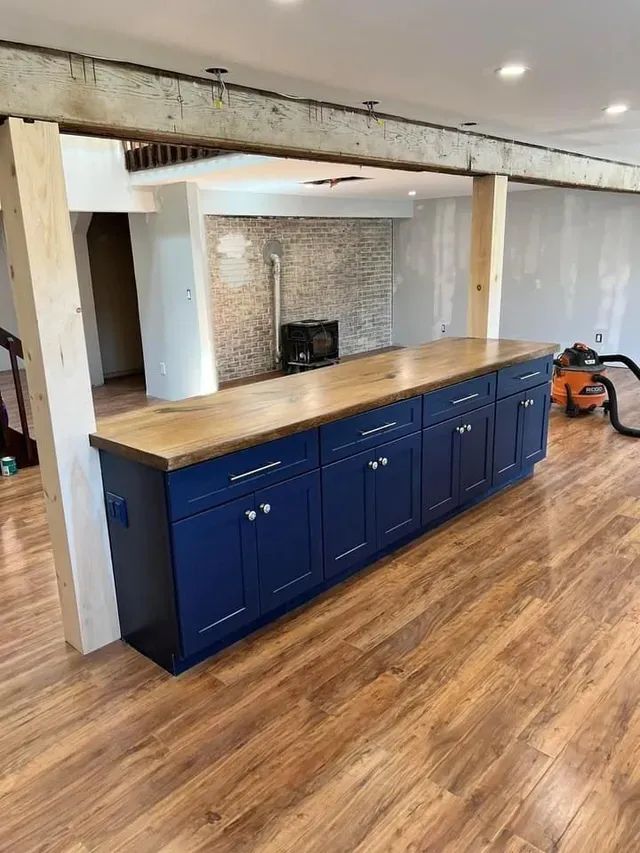 Blue kitchen island with wooden countertop and cabinets, in a room with hardwood floors and exposed beams.