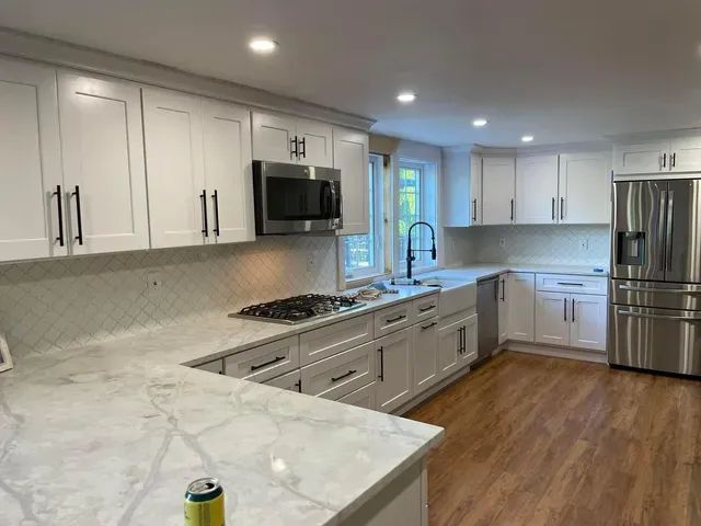 White kitchen with quartz countertops, cabinets, stainless steel appliances, and wood flooring.