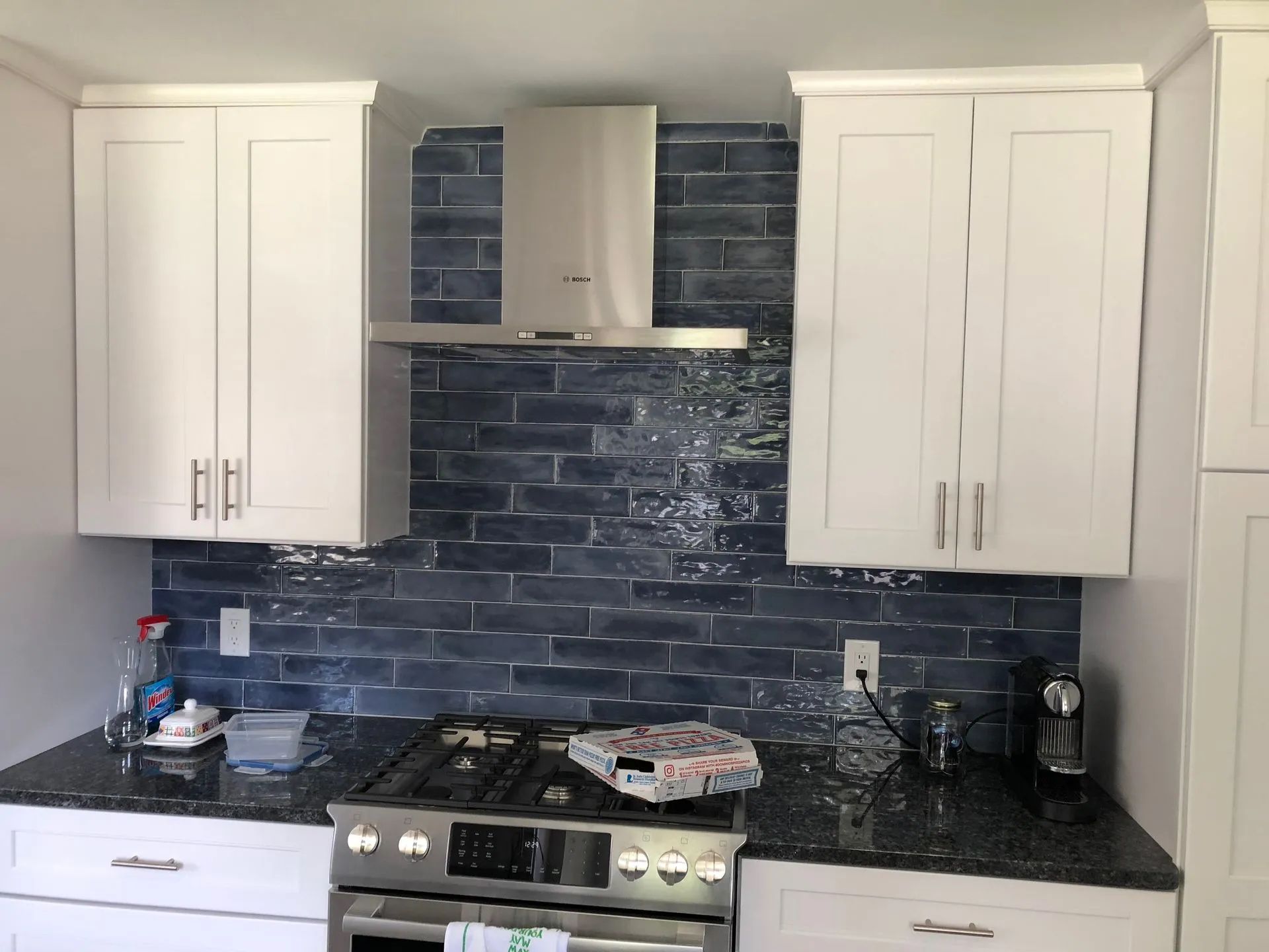 White kitchen cabinets with blue tiled backsplash above a black granite countertop and stainless steel stove.