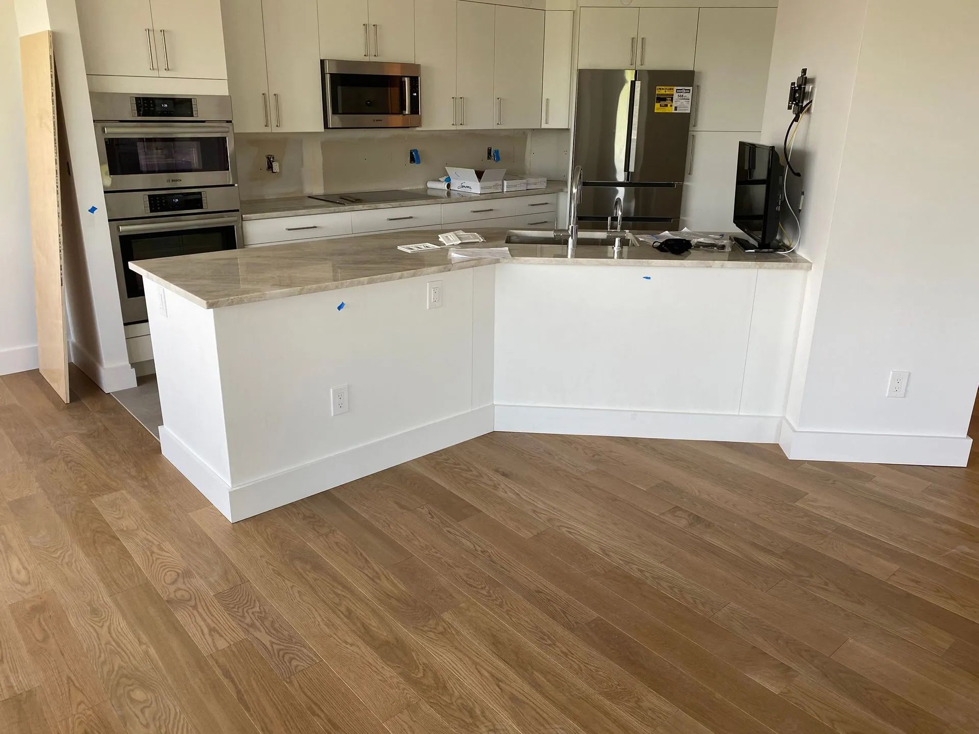 Kitchen with white cabinets, beige countertops, stainless steel appliances, and wood floors.