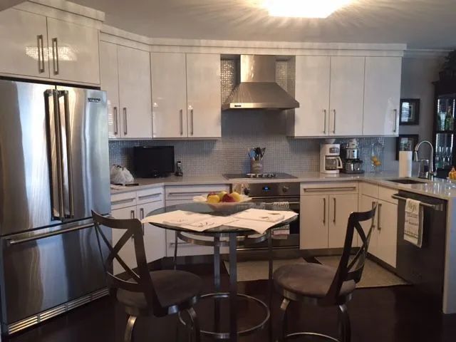Bright white kitchen with stainless steel appliances, breakfast table with two chairs.