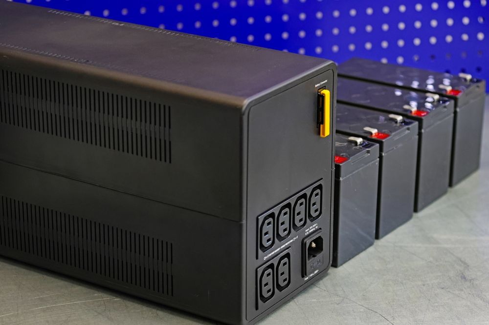 A row of batteries are sitting next to a black ups.