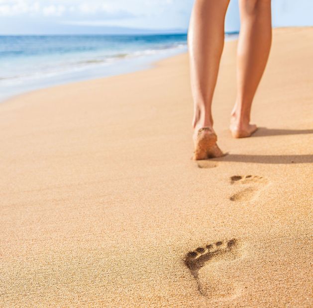 Eine Frau geht am Strand spazieren und hinterlässt Fußabdrücke im Sand.