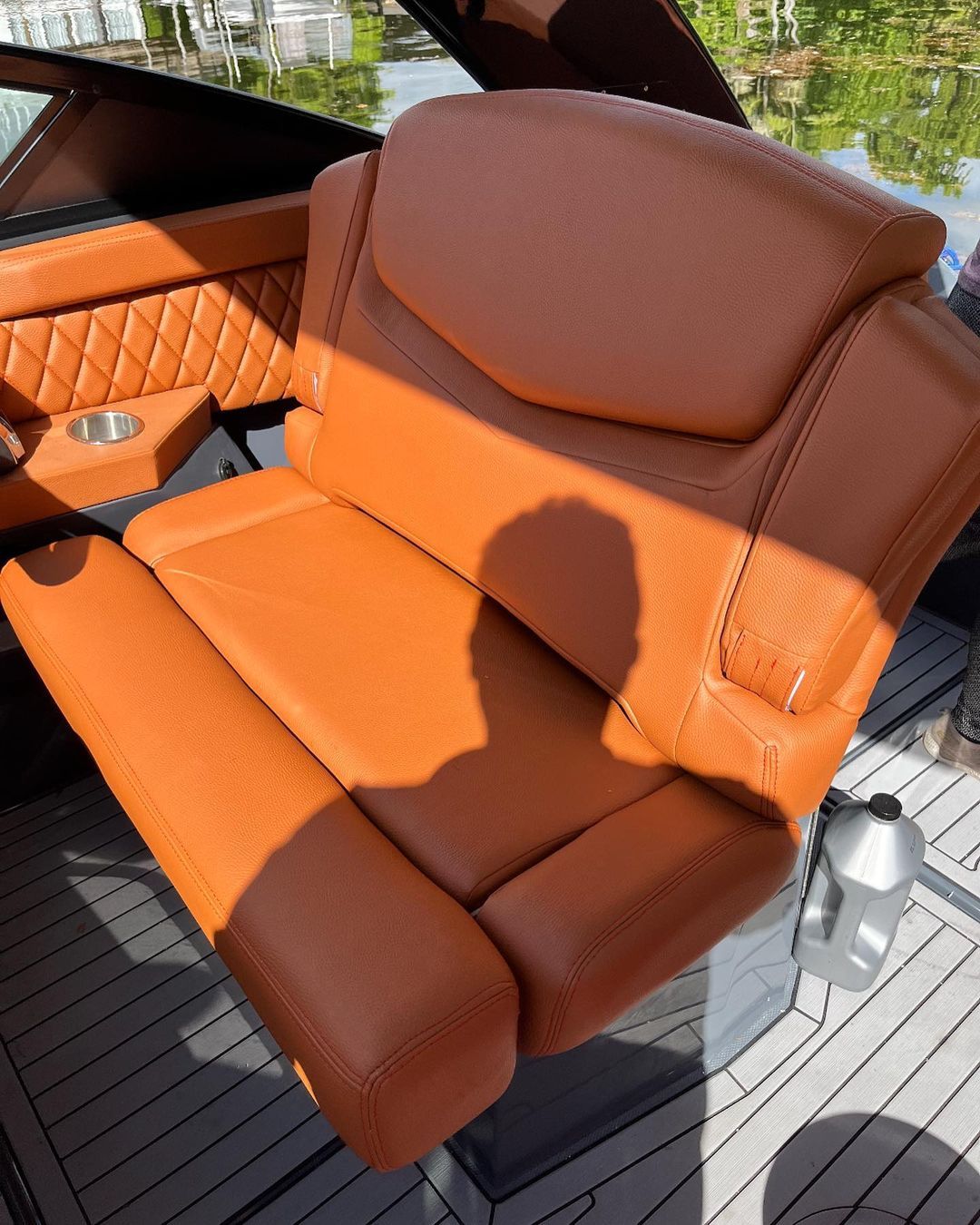 A brown leather seat on a boat is sitting on a wooden deck.
