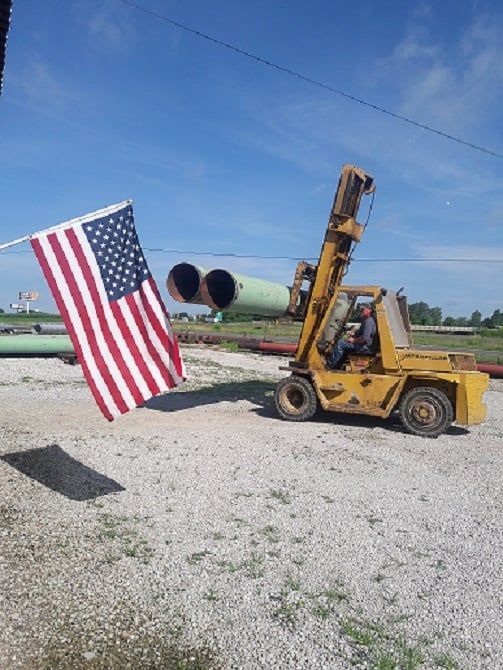 A yellow forklift is carrying a large American flag — Odessa, MO — Continental Pipe Co.
