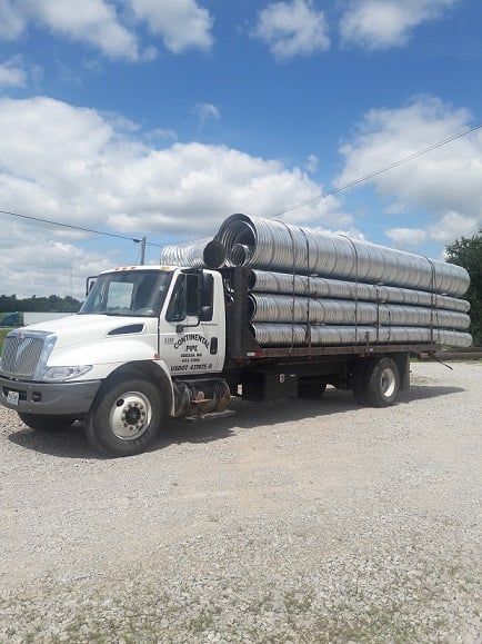 A white truck is carrying a stack of pipes on a gravel road — Odessa, MO — Continental Pipe Co.
