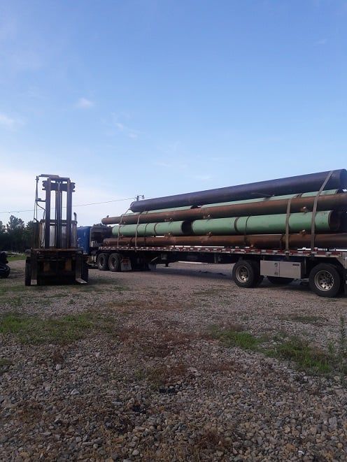 A truck is carrying a stack of pipes on a gravel road — Odessa, MO — Continental Pipe Co.