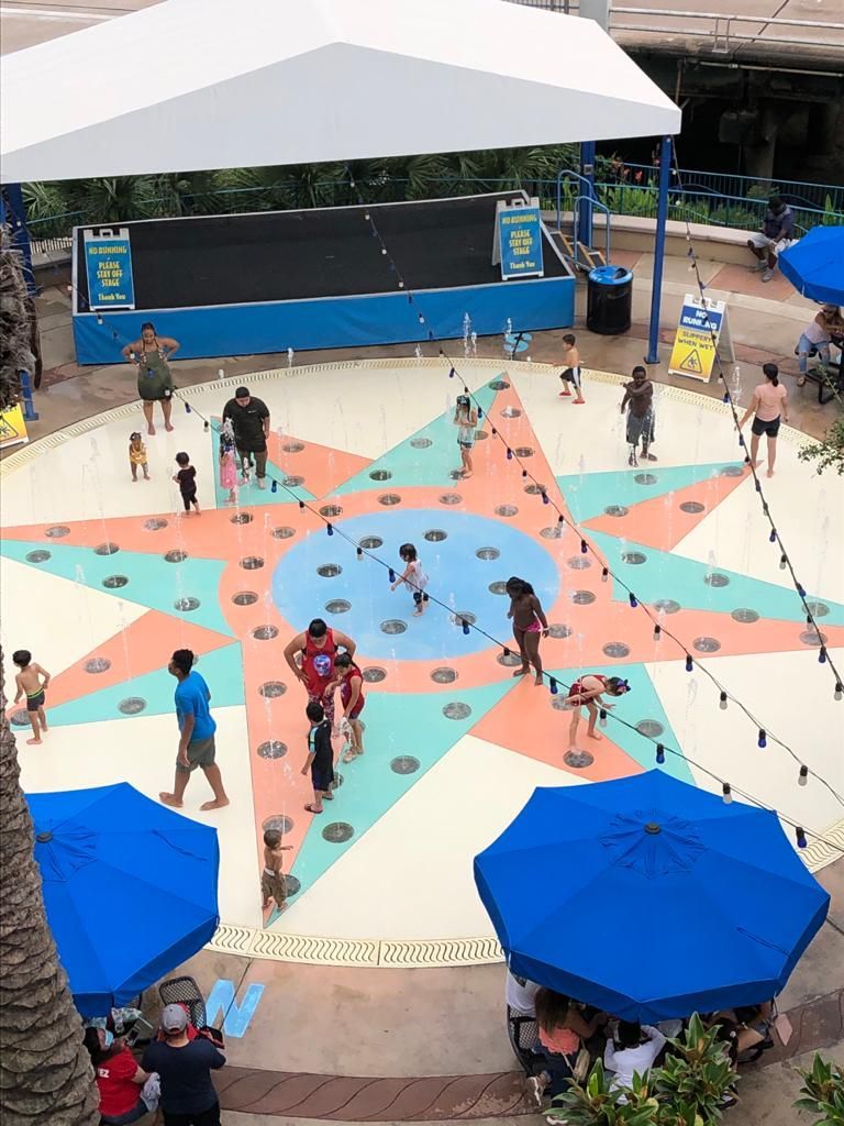A group of people are playing on splash pad with umbrellas