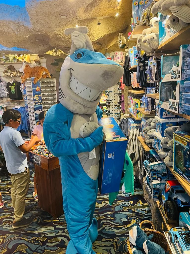 A man in a shark costume is holding a box in a store