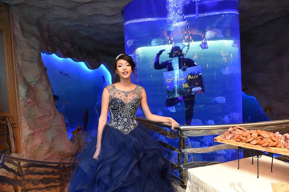 A woman in a blue dress stands in front of an aquarium