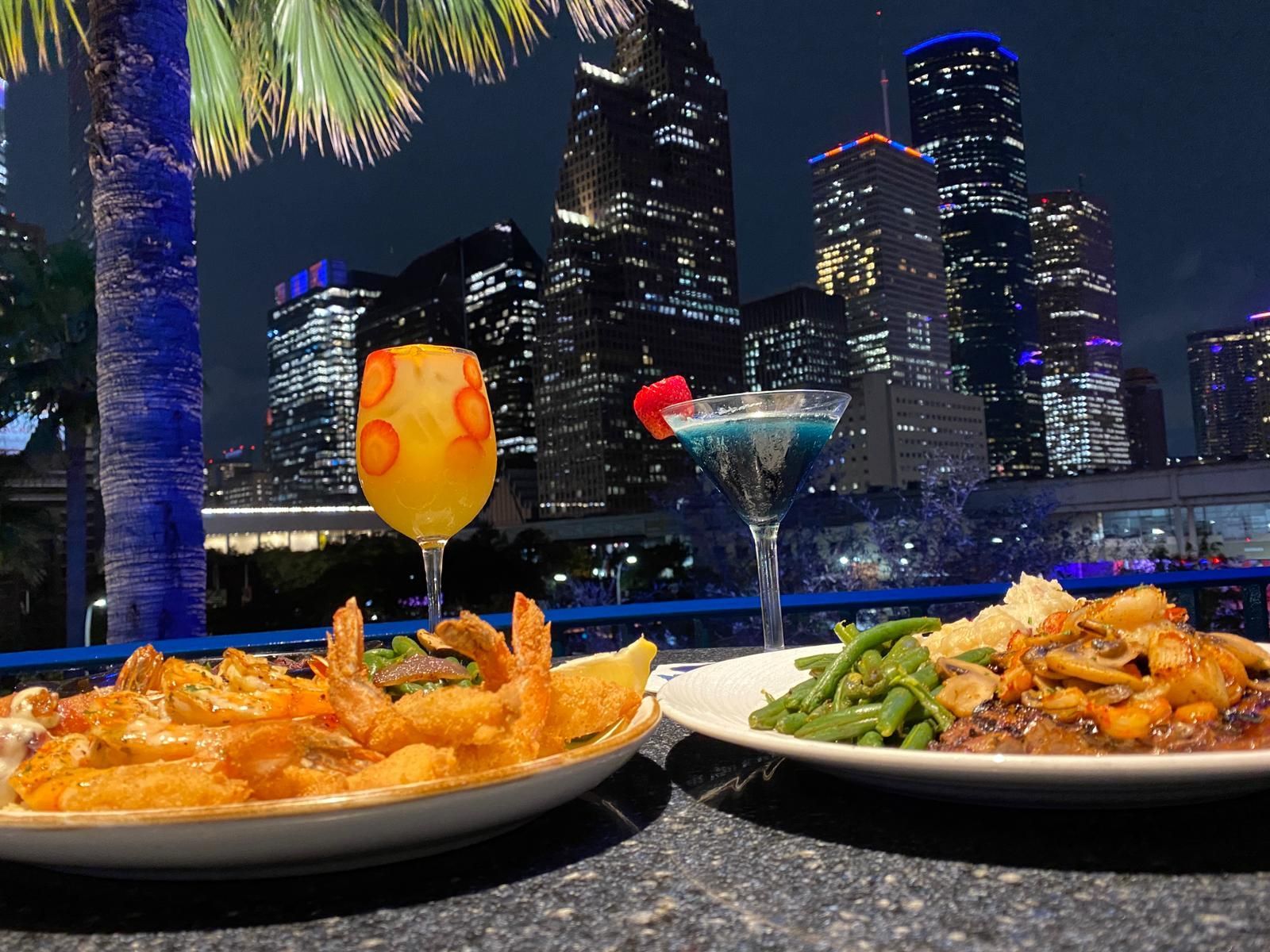 Two plates of food and a drink with a city skyline in the background
