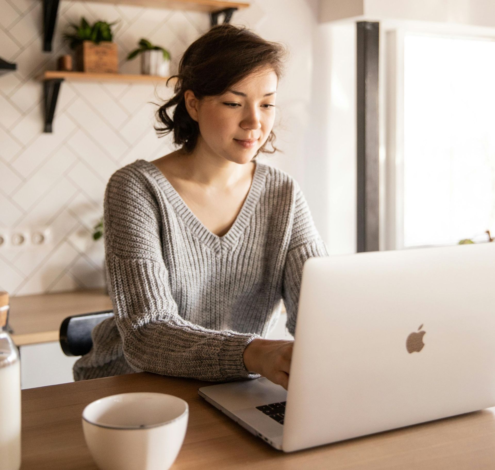 A woman is sitting at a table using an apple laptop