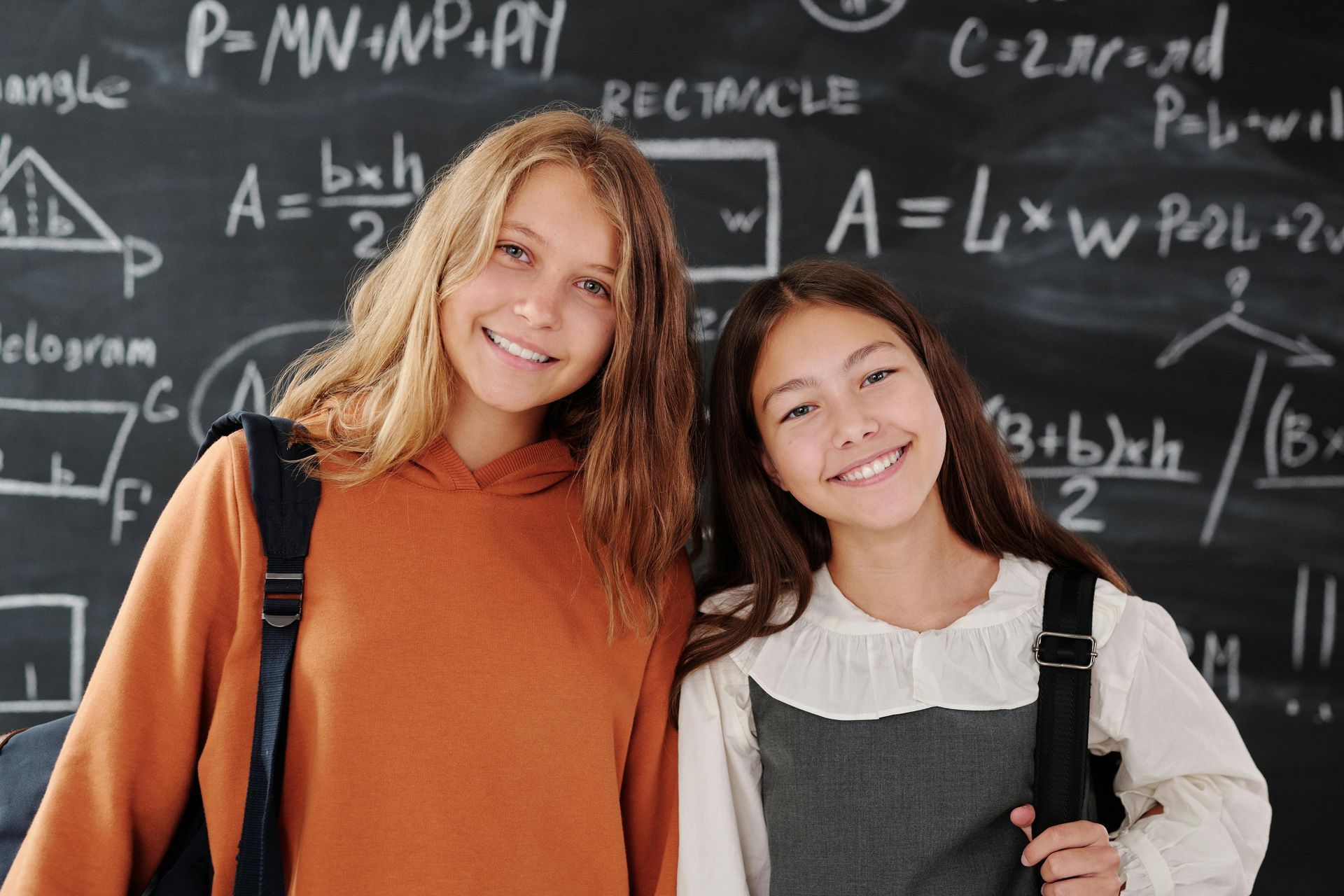 Two girls standing in front of a blackboard with math equations on it