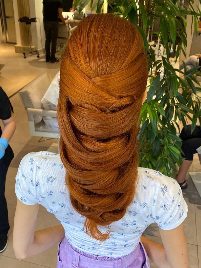 Una persona con i capelli color rame, acconciati in una coda di cavallo voluminosa e ondulata, vista di spalle in un salone di bellezza.