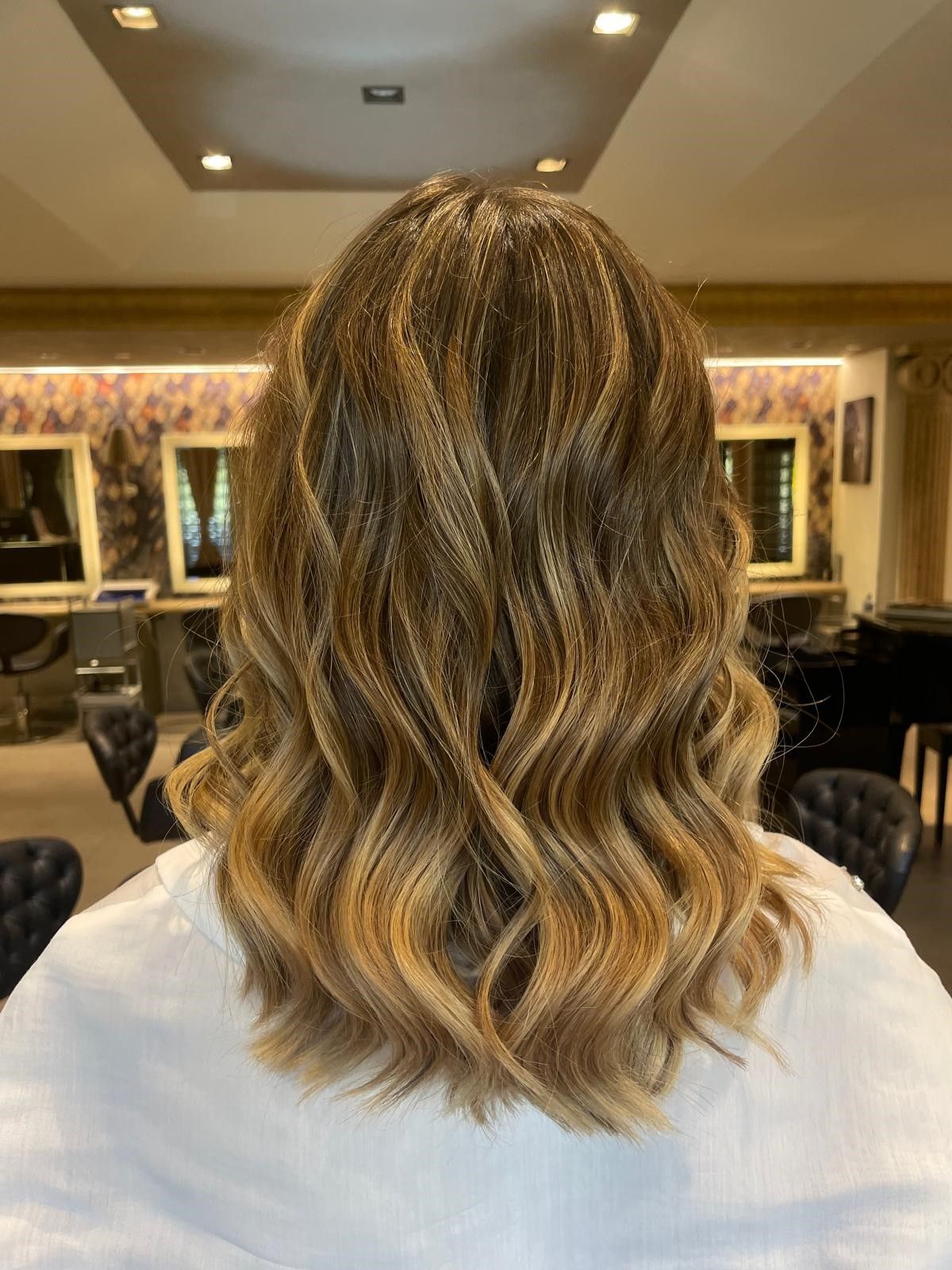 Capelli di media lunghezza con morbidi ricci ondulati e una colorazione ombré dal castano al biondo, in un salone di parrucchiere.