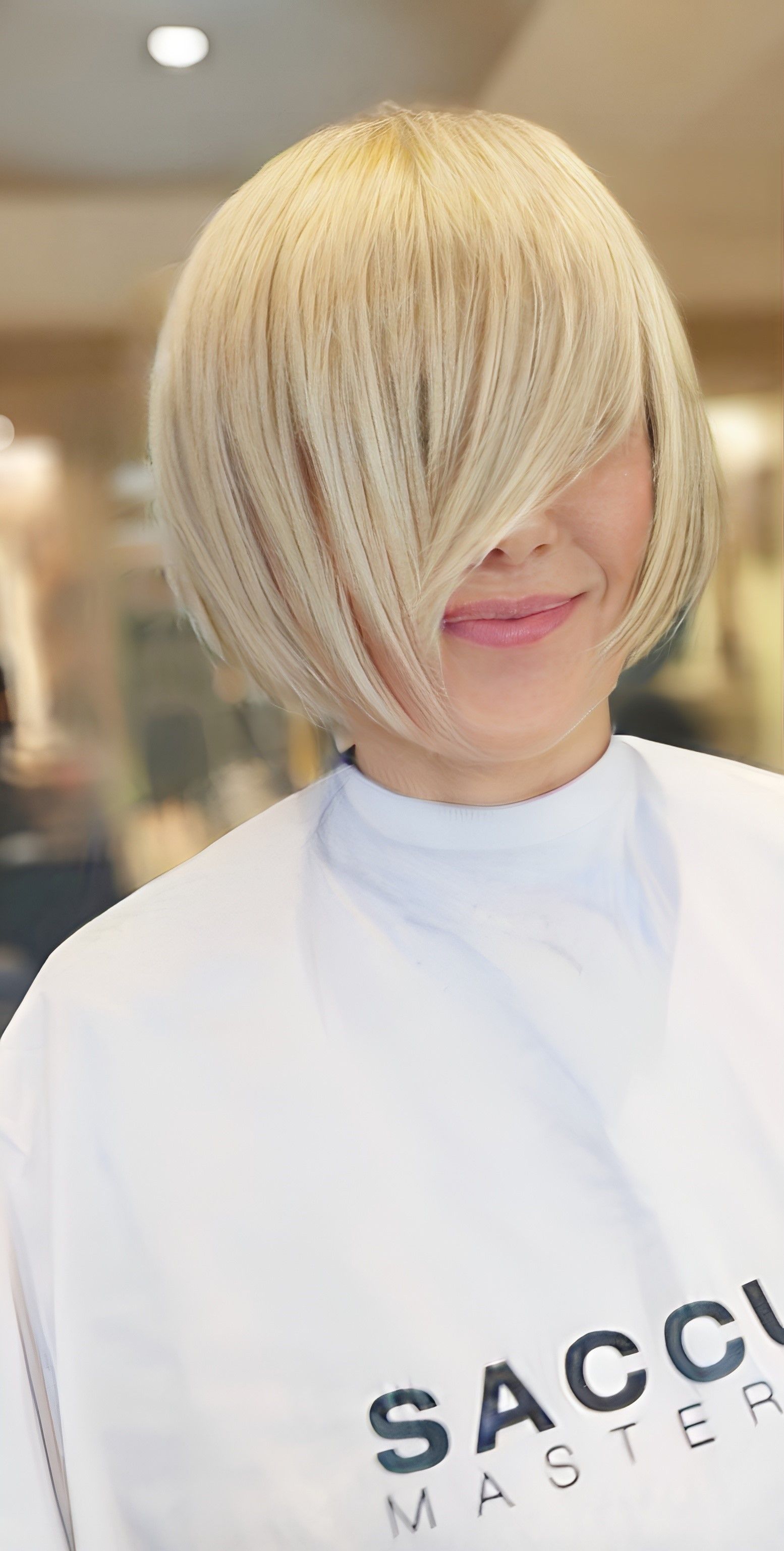 Una persona con i capelli biondo platino lunghi fino alle spalle, tagliati a caschetto scalato con la frangia che copre un occhio, sorridente.