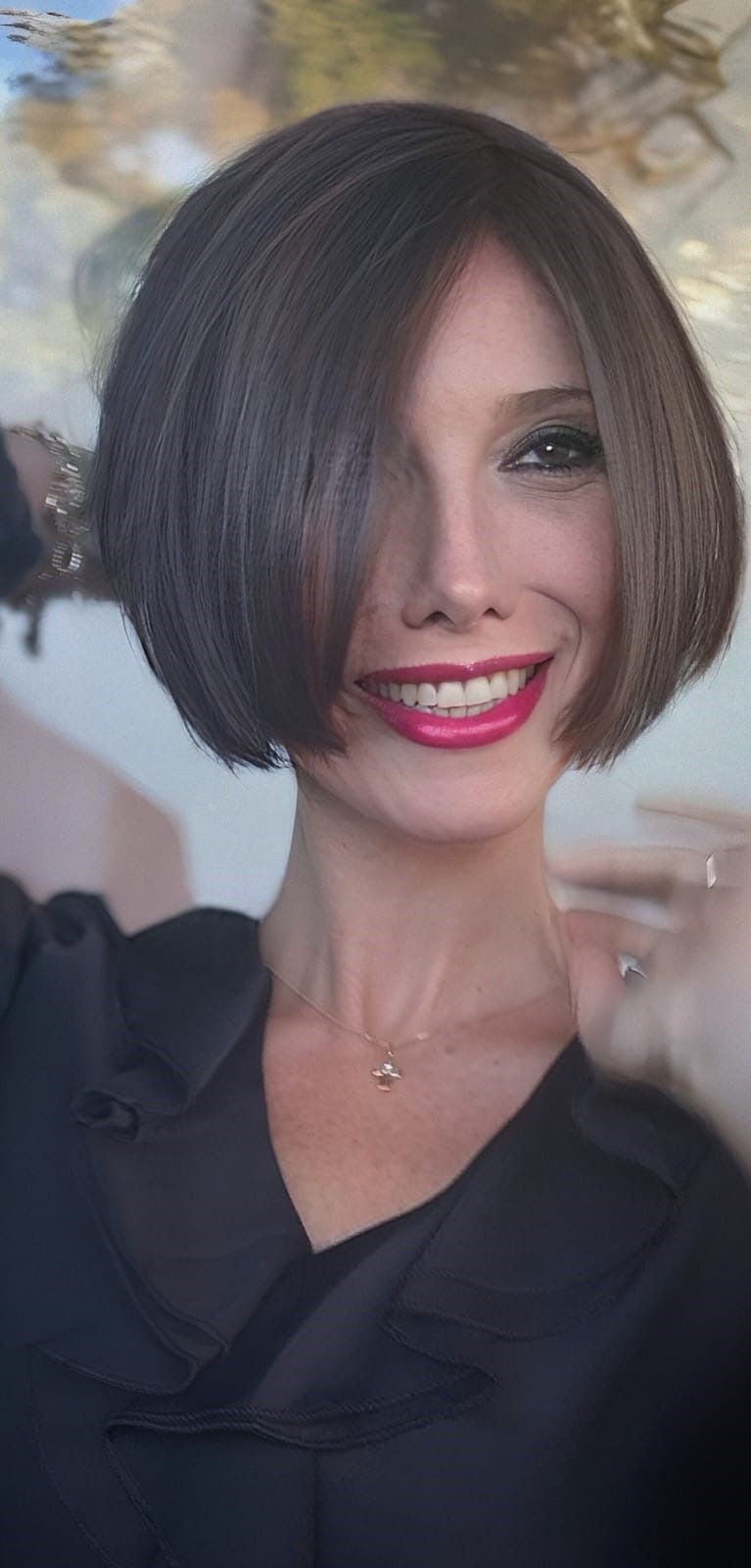 Una persona con un caschetto castano all'altezza del mento e un rossetto rosso acceso sorride mentre indossa una camicetta scura con scollo a V.