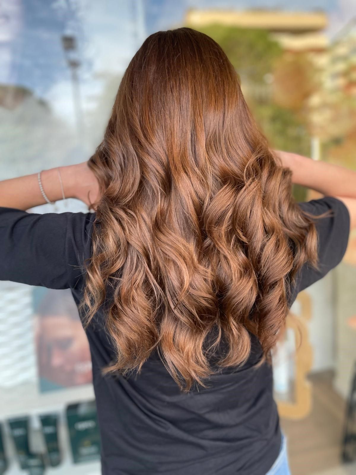 Una persona vista di spalle mostra lunghi capelli mossi color castano in un salone di bellezza.