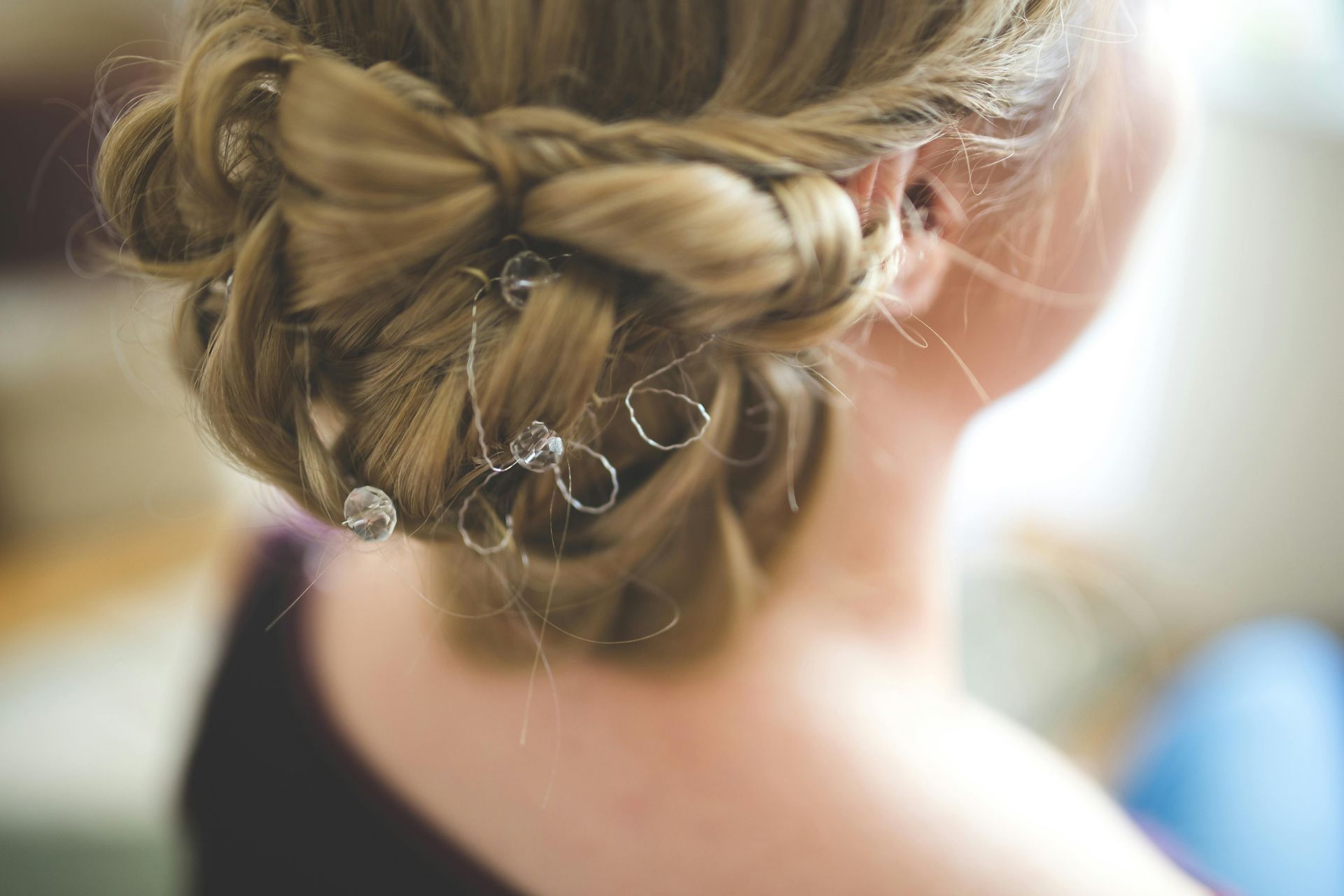 Primo piano di un'acconciatura bionda con chignon basso intrecciato, adornata con piccole forcine di cristallo trasparente.