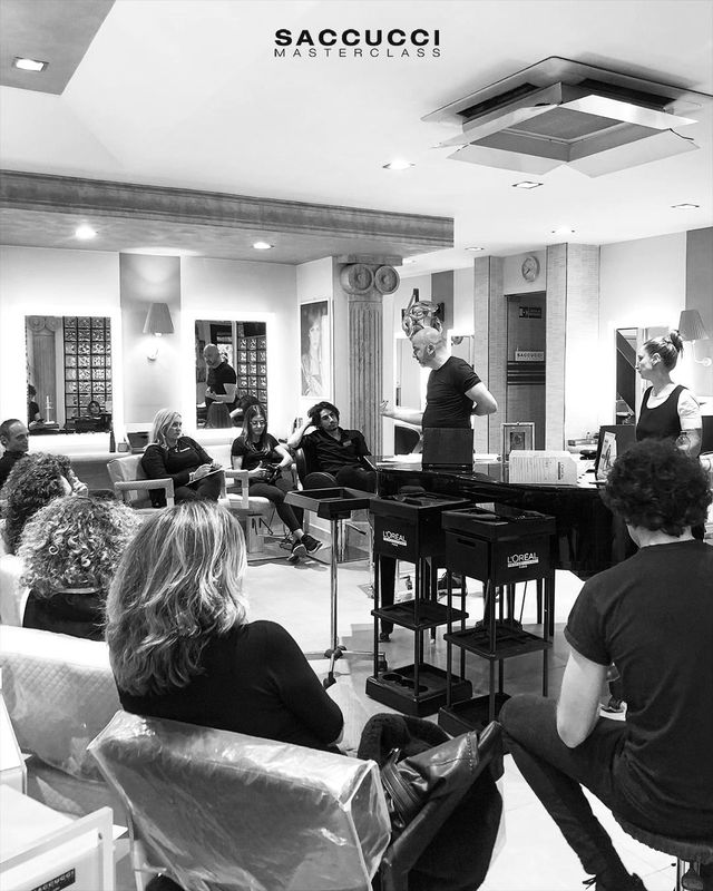Un gruppo di persone ascolta un istruttore durante un seminario didattico sull'acconciatura in un salone professionale.