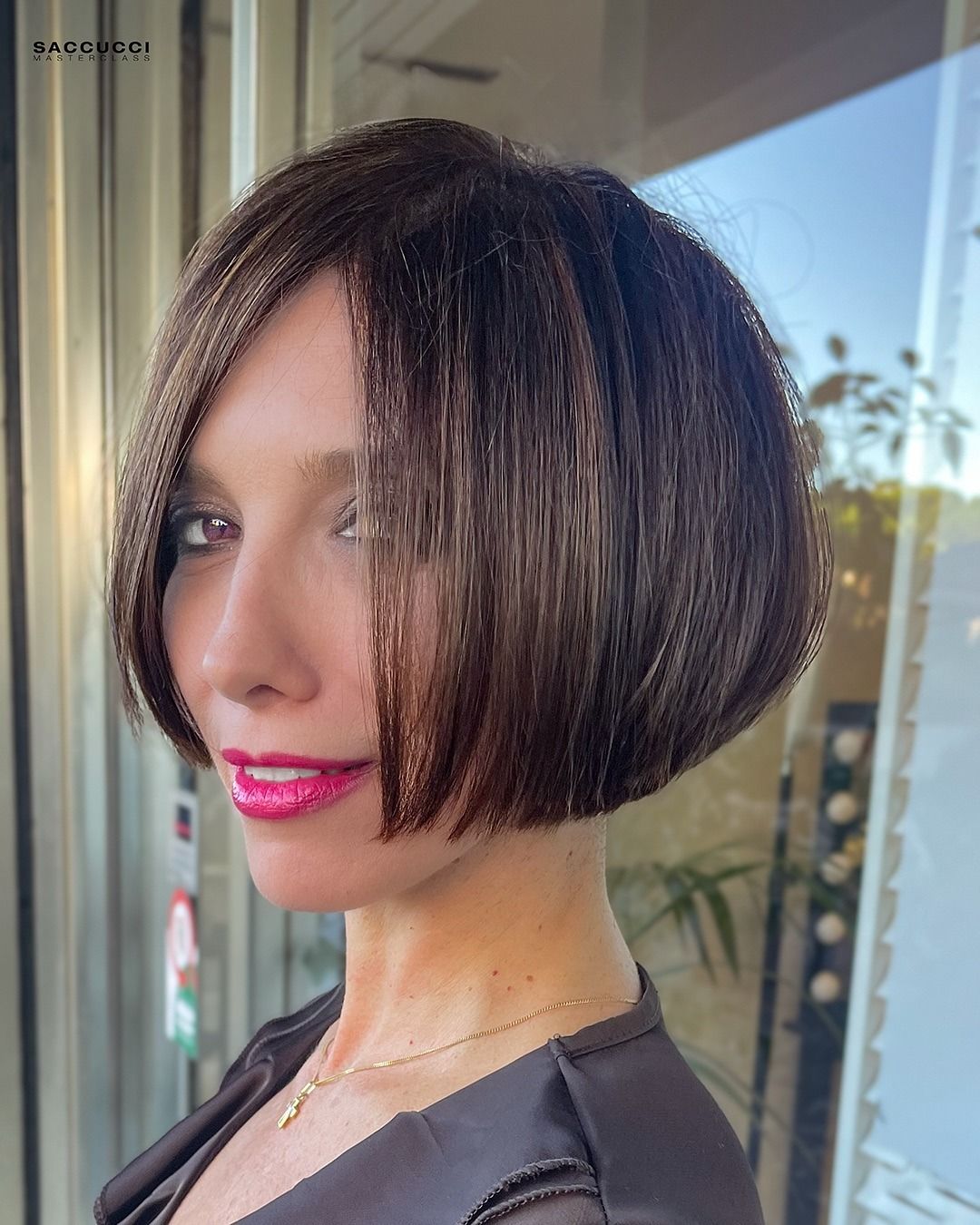 Una persona con un caschetto scuro e scalato e un rossetto rosa acceso posa davanti a una finestra.