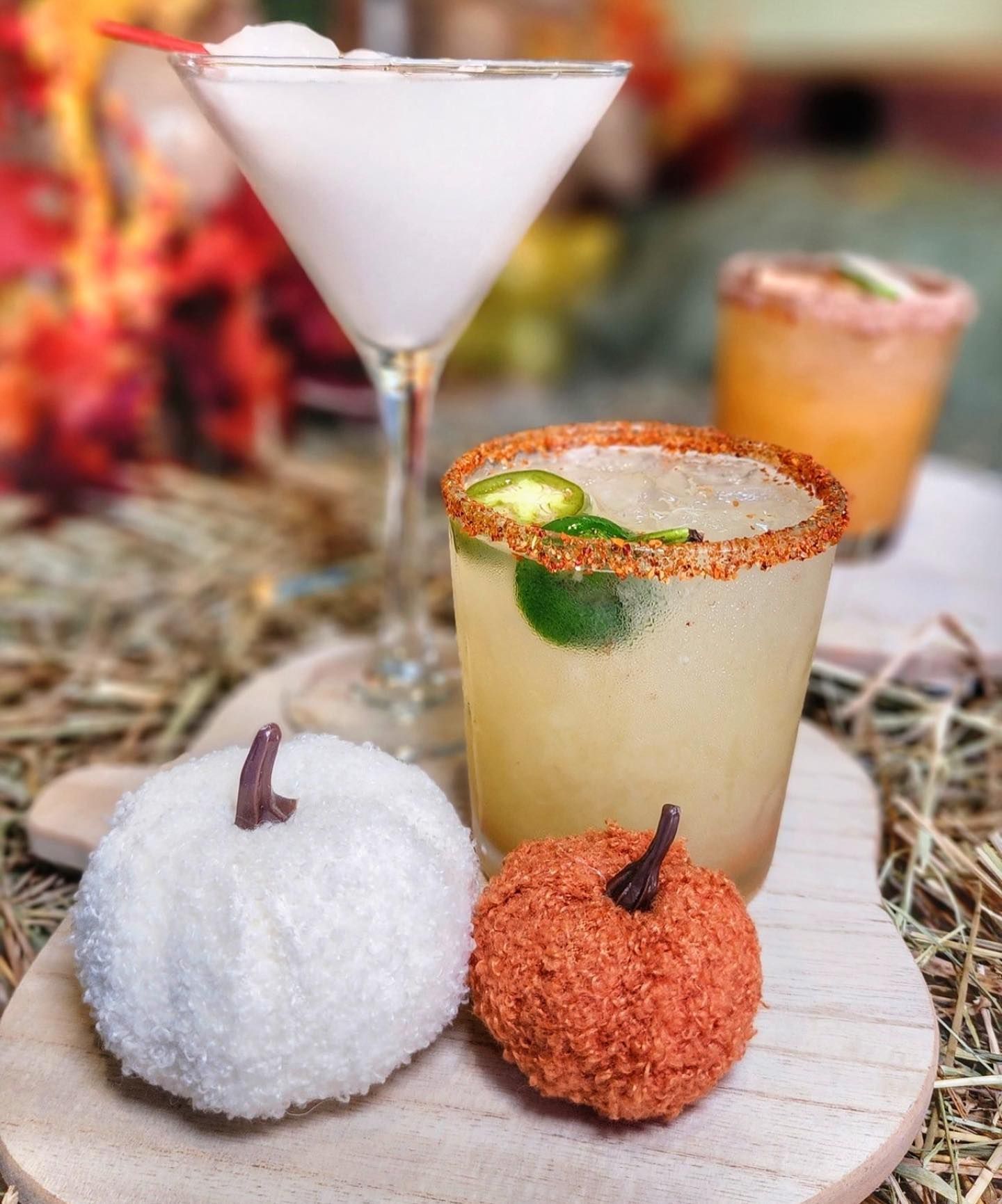 Cocktails on wooden board, with white and orange pumpkin decor. Includes a margarita.