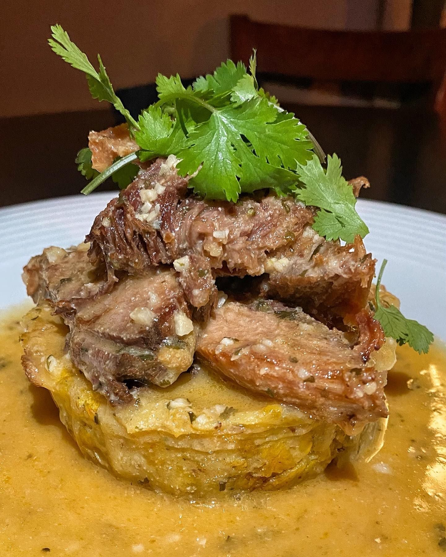 Braised meat with garlic sauce atop a fried plantain, garnished with cilantro.