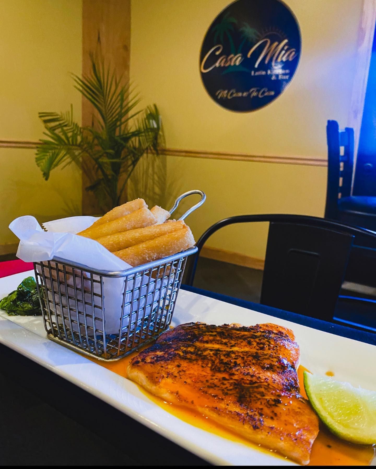 Salmon dish with churros in a wire basket, lime, and Casa Mia restaurant logo in background.