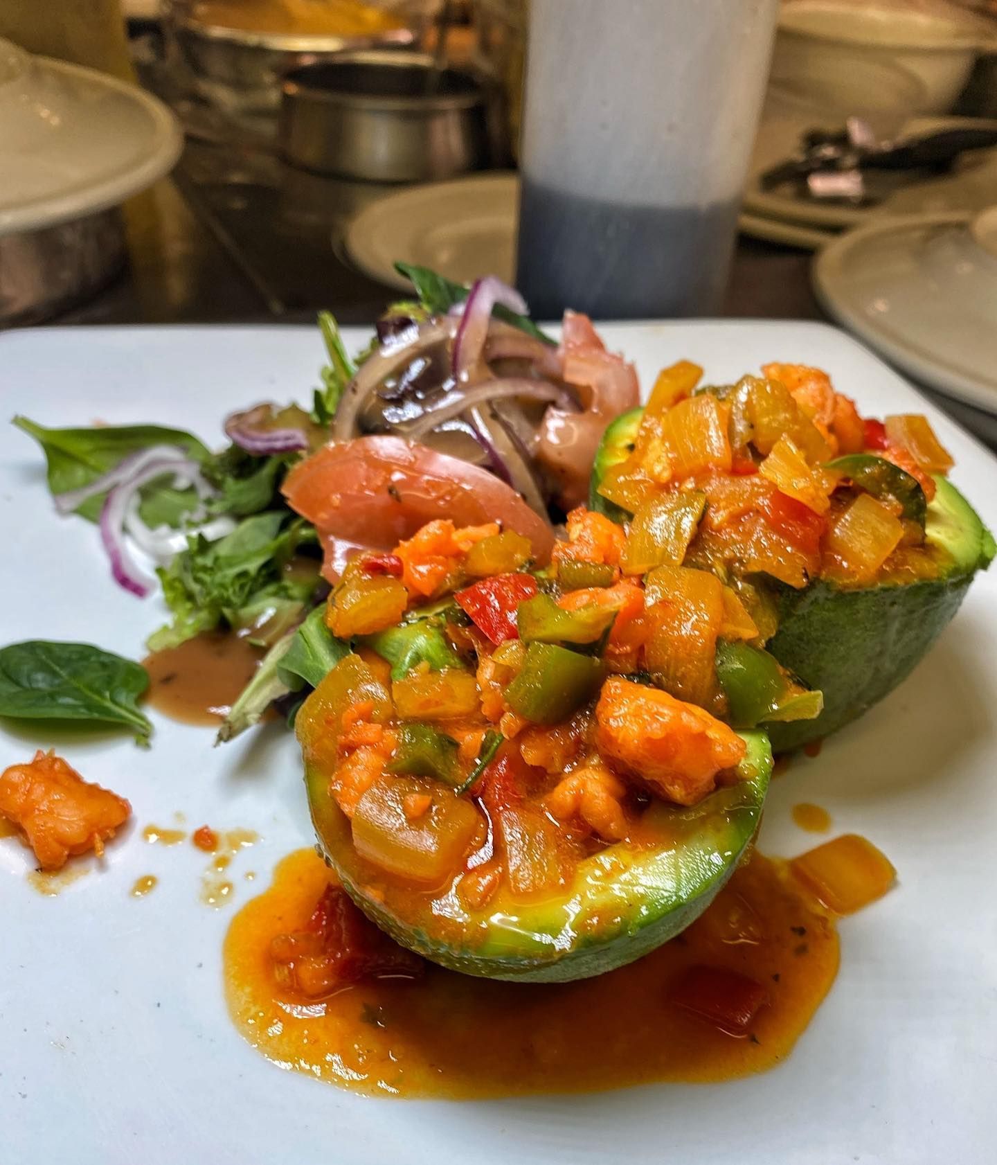 Stuffed avocado halves with colorful vegetable mixture and side salad on a white plate.