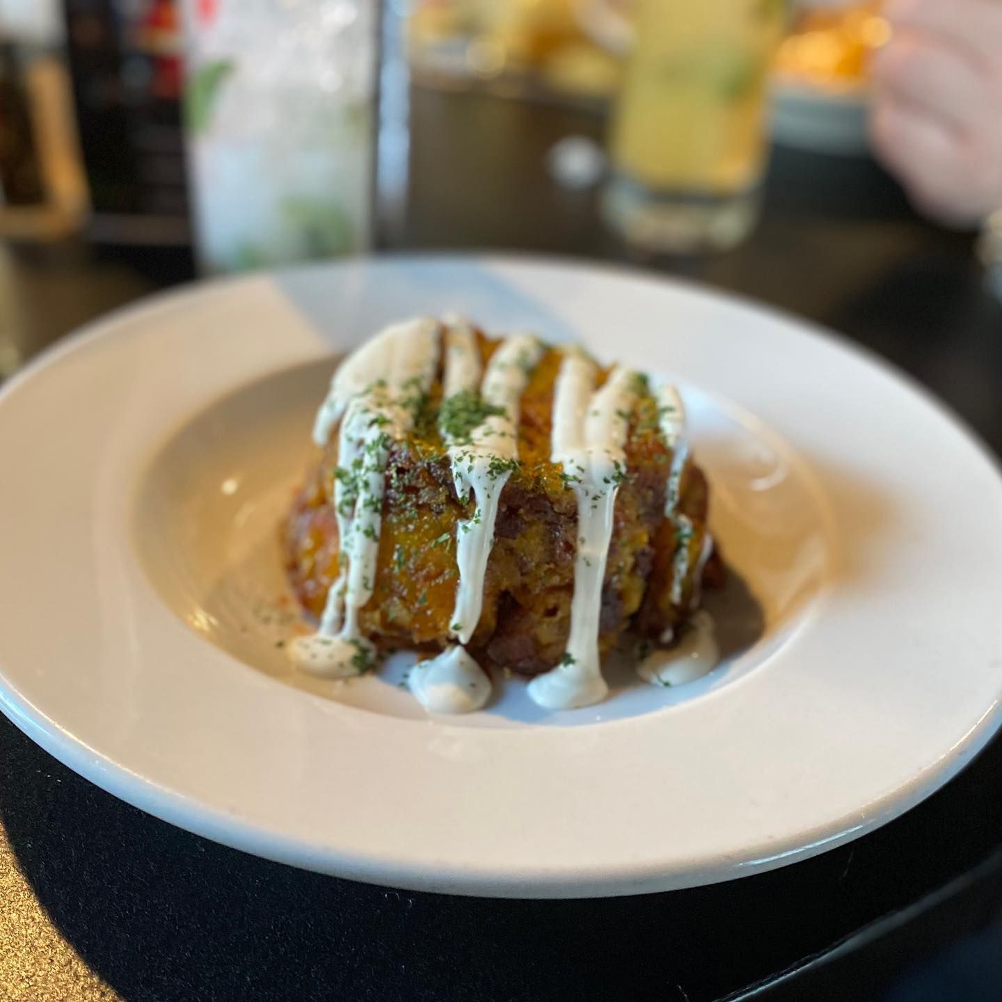 A savory golden-brown food item, drizzled with white sauce, on a white plate.