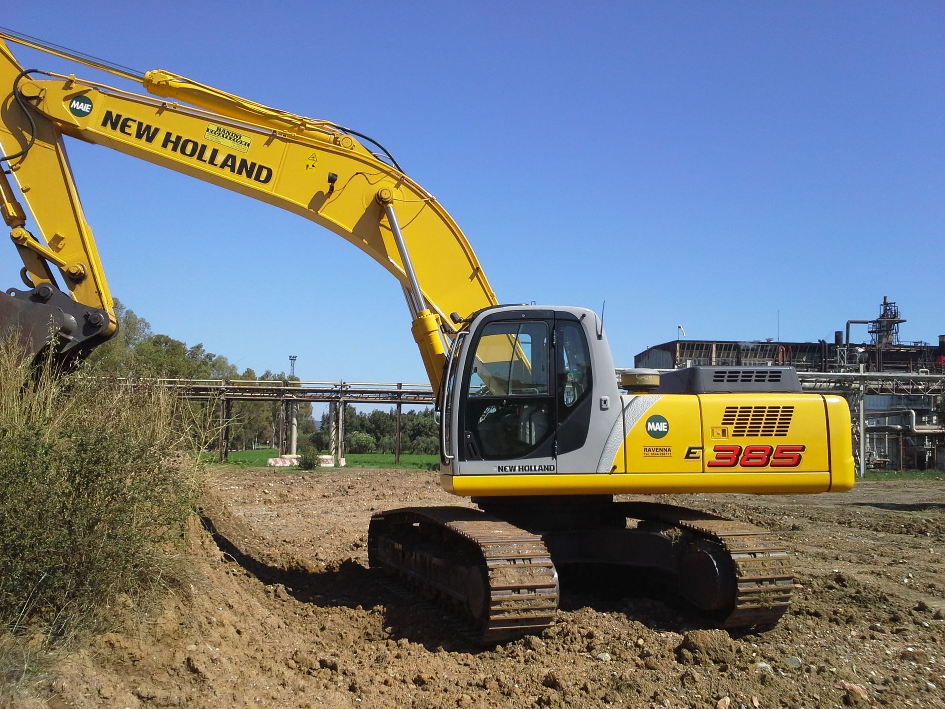 Un escavatore giallo New Holland su cingoli in un cantiere edile sotto un cielo azzurro.