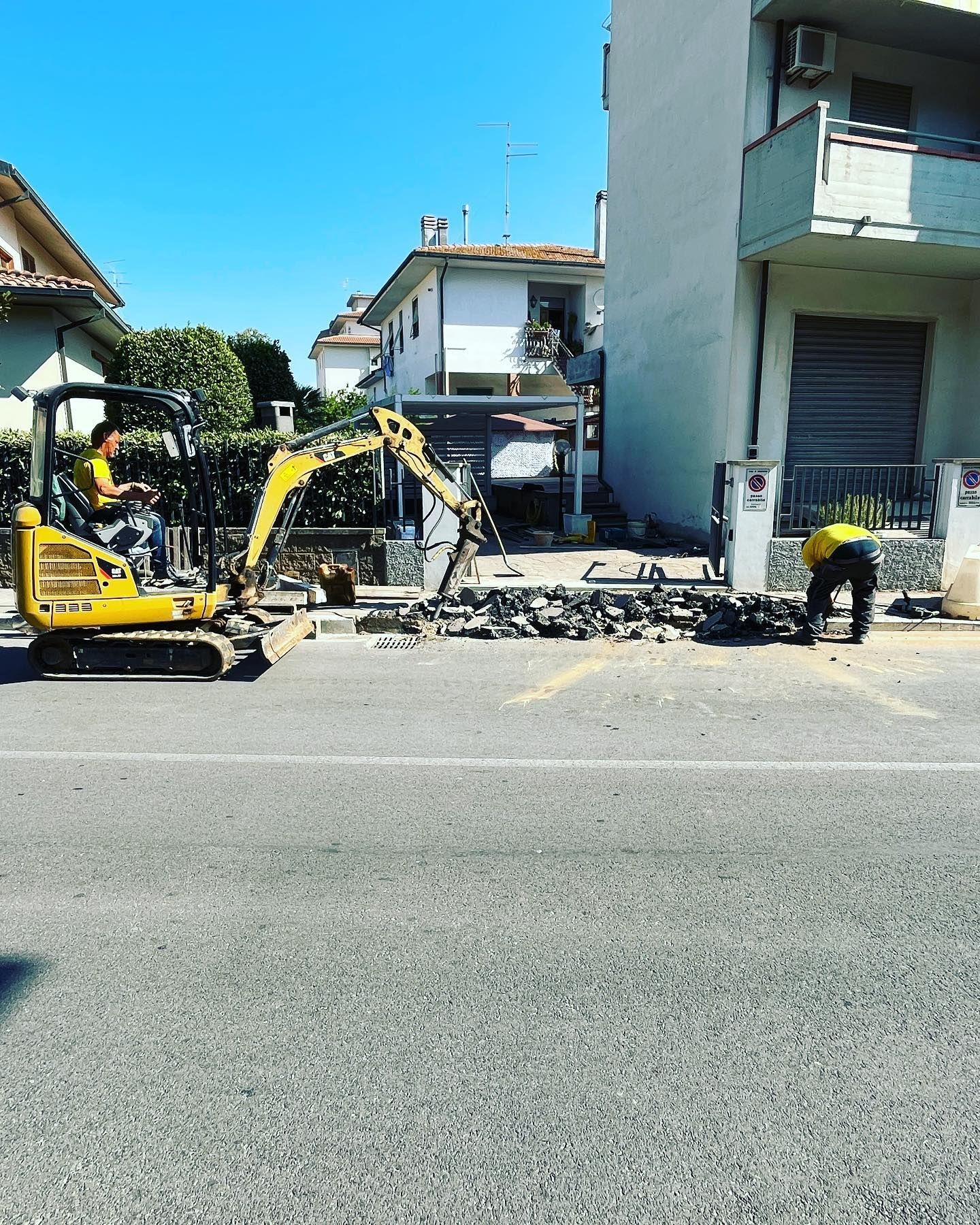 Due escavatori gialli e operai rimuovono le macerie in una strada residenziale accanto alle case.
