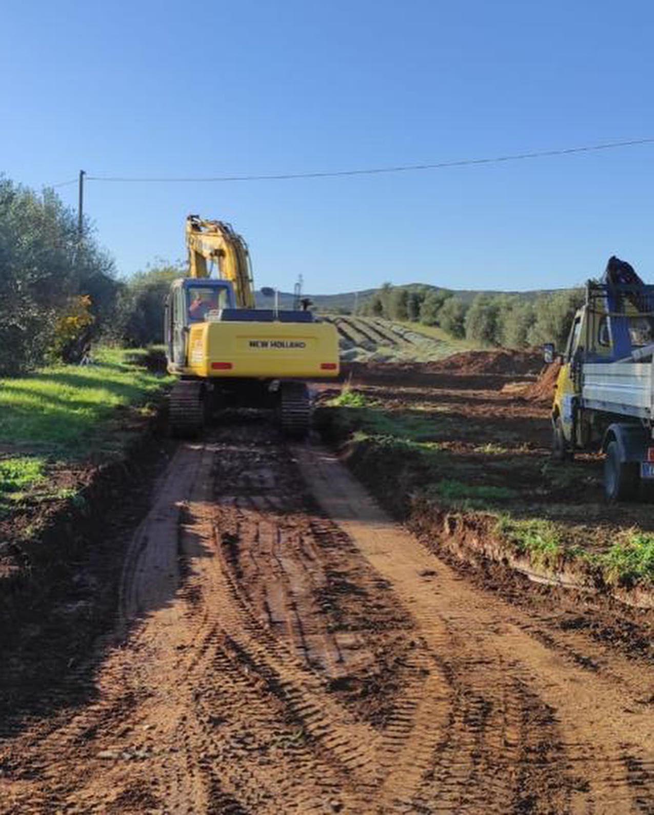 Un escavatore giallo su una strada sterrata in un cantiere rurale sotto un cielo azzurro e limpido.