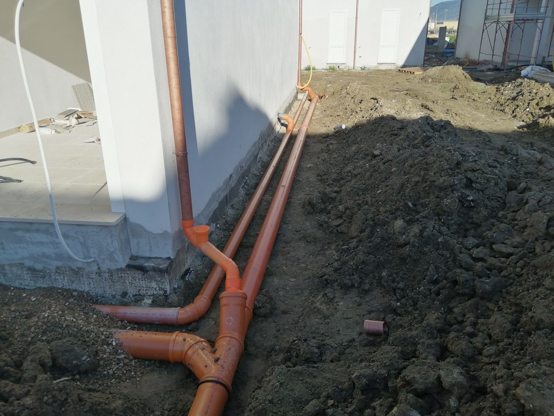Tubi arancioni posati in una trincea accanto alle fondamenta di un edificio durante la costruzione.