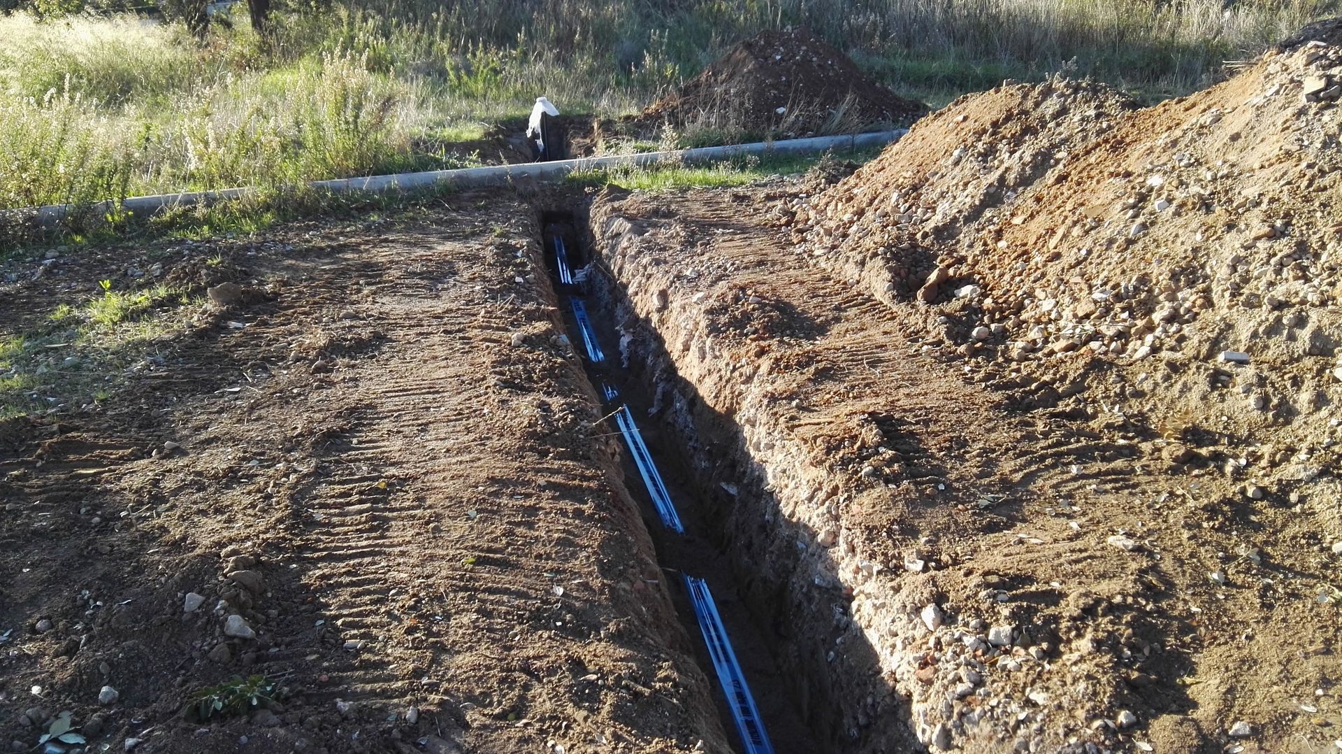 Un tubo di irrigazione nero passa attraverso una trincea di terra accanto a un cumulo di terra scavata all'aperto.