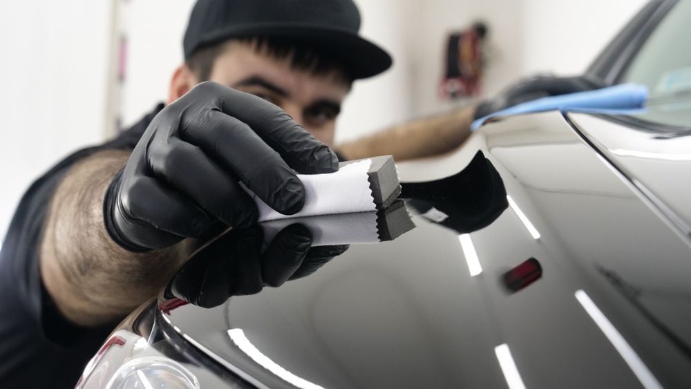 A man in black gloves is polishing a black car.