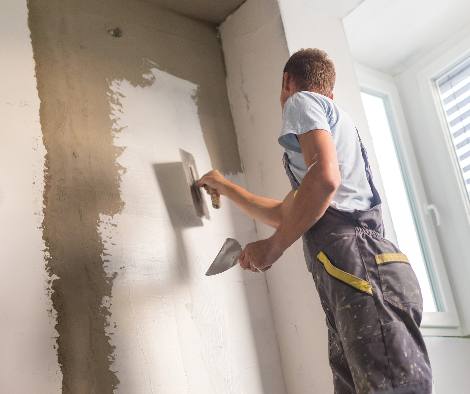 A man is plastering a wall with a trowel.