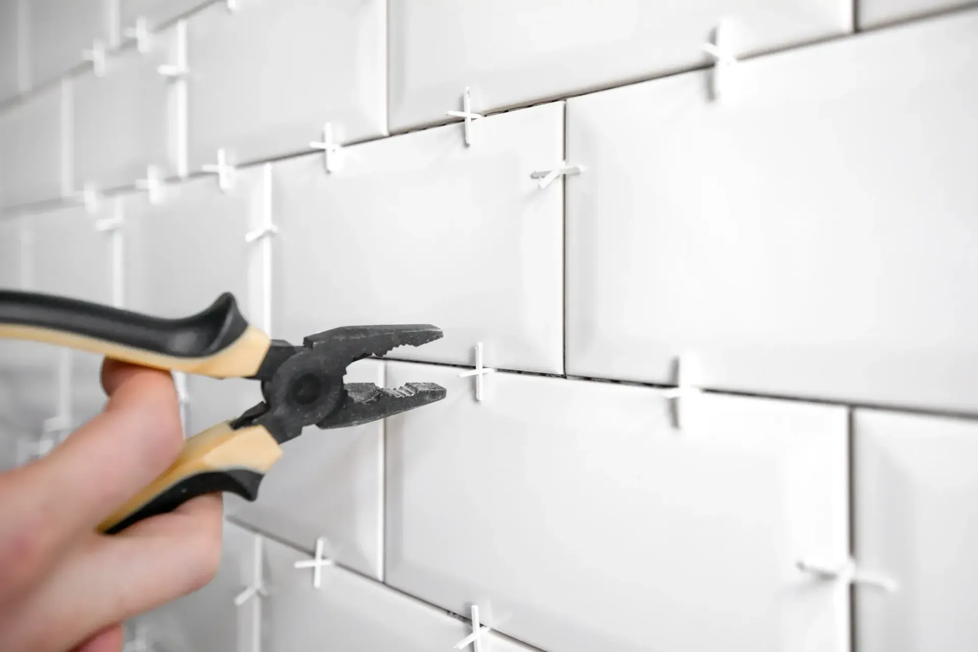 A person is using pliers to install tiles on a wall.