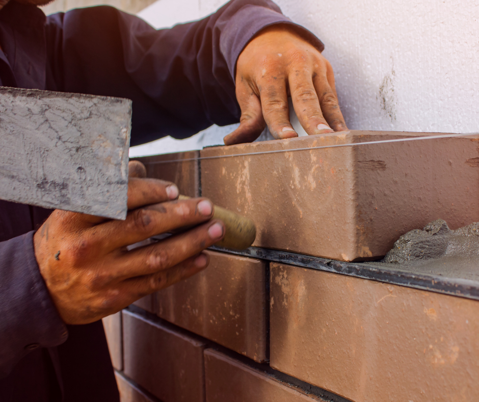A man is laying bricks on a wall with a trowel.